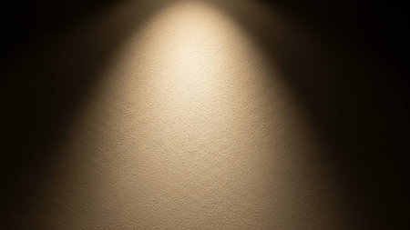 A textured wall is illuminated by a single, warm spotlight creating a bright central glow and dark shadows.の素材