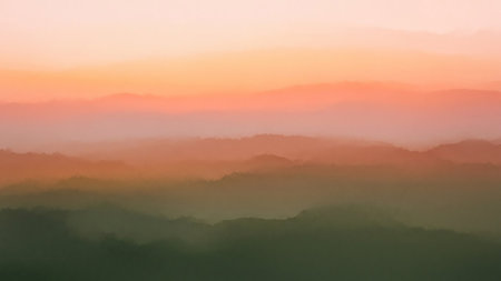 Layers of misty mountains fade into soft hues of orange, pink, and green, creating an atmospheric and tranquil landscape at sunrise or sunset.の素材