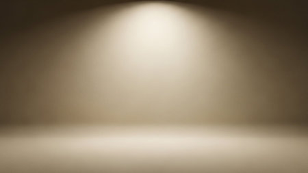 An empty studio background with a soft, warm spotlight creating a gradient of light and shadow on a neutral beige surface.の素材