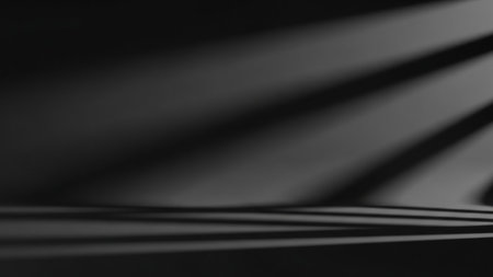 An abstract, dark background with a smooth gradient from black to dark gray. Dramatic, sweeping shadows are cast across the surface, creating a sense of depth and form. The lighting is soft and indirect, emphasizing the interplay of light and shadow.の素材