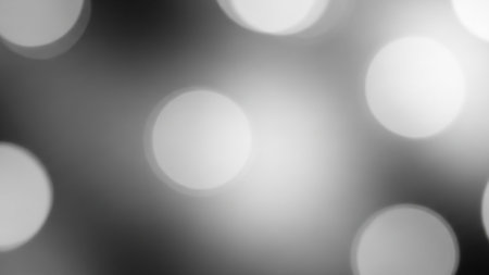 A grayscale abstract background featuring soft, blurred circles of light creating a bokeh effect with a bright glow in the center.の素材