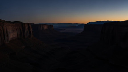 A vast canyon landscape at dusk with towering rock formations casting deep shadows and a glowing horizon in the distance.の素材