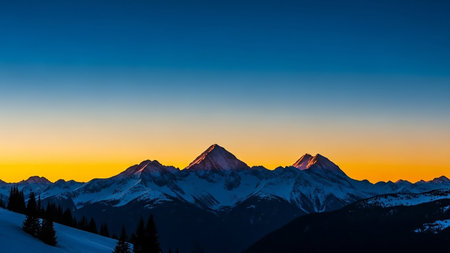 Snow-covered mountain peaks are bathed in the warm glow of a golden sunrise against a clear blue sky.の素材