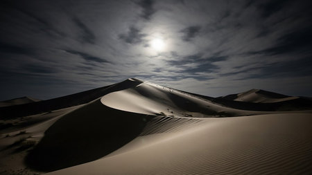 A desert landscape at night with large sand dunes illuminated by moonlight, casting dramatic shadows under a cloudy sky.の素材