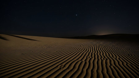 Rippled sand dunes stretch across a dark desert landscape under a clear night sky filled with stars.の素材