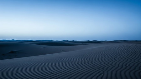 Gentle sand dunes with rippling textures stretch across the landscape under a clear blue twilight sky.の素材