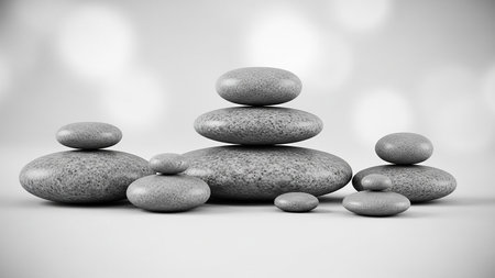 A monochrome studio shot of several smooth, grey zen balancing stones stacked in a harmonious arrangement on a clean white background.の素材