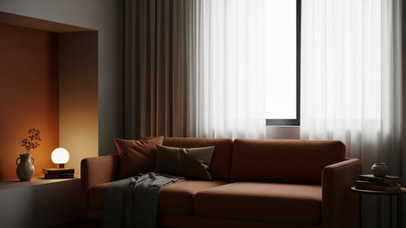 A rust-colored sofa is illuminated by warm light, with a checkered blanket draped over it and a minimalist side table nearby.の素材