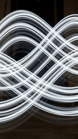 An abstract composition of intertwined white light trails creating a symmetrical, flowing pattern against a dark, blurred background.の素材