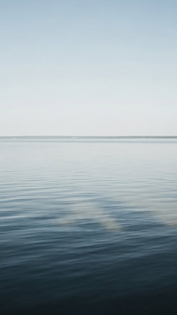 A minimalist view of calm, rippling blue water under a pale, clear sky with a subtle horizon line.の素材