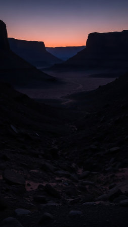 A deep canyon carved by nature, with towering dark rock formations silhouetted against a faint orange twilight sky at dusk.の素材
