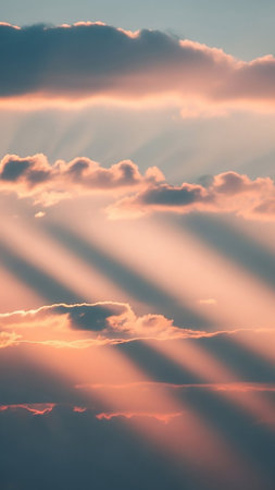 Dramatic crepuscular rays pierce through pink and blue clouds during a sunset, casting ethereal light across the sky.の素材