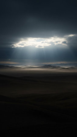 Rays of sunlight pierce through dark, heavy clouds, illuminating a hazy, layered desert landscape with distant mountains.の素材