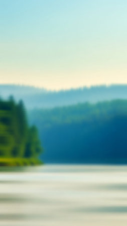 An impressionistic, softly blurred image of a tranquil lake with distant forested hills under a pale sky.の素材