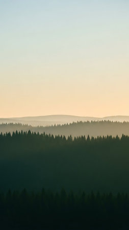 Layered silhouettes of forested hills recede into the distance under a soft, hazy sky at sunrise, creating a serene and atmospheric landscape.の素材