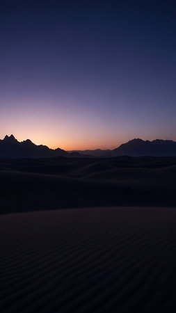 Gentle rolling sand dunes are silhouetted against a twilight sky transitioning from deep purple to a soft orange, with distant mountains on the horizon.の素材