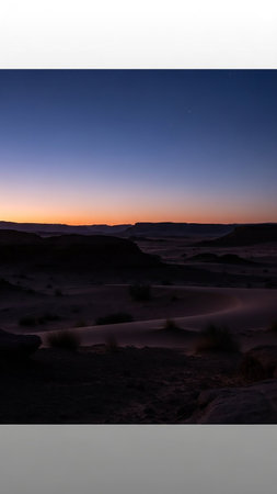 A serene desert landscape at dusk with rolling hills silhouetted against a gradient sky of deep blue and warm orange.の素材