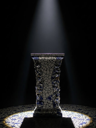 An ornate pedestal covered in blue and white mosaic tiles is dramatically lit by a spotlight against a dark background.の素材