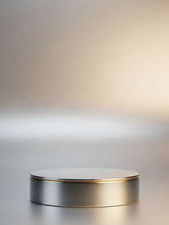A sleek silver cylindrical podium with a subtle gold trim rests on a reflective metallic surface under soft, diffused lighting.の素材
