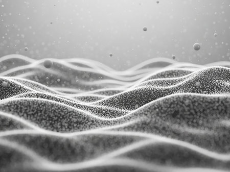 A grayscale macro view of a textured, undulating surface covered in small particles and scattered spheres, with soft lighting.の素材
