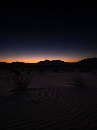A serene desert landscape at dusk, with rippled sand dunes in the foreground and a dark mountain silhouette against a gradient twilight sky.の素材