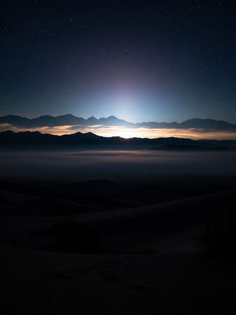 A dark and atmospheric desert landscape at night, with silhouetted mountains under a starry sky and a soft glow on the horizon.の素材