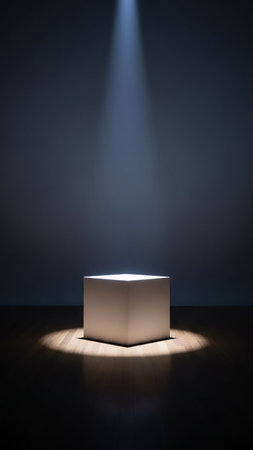 A simple white cube pedestal sits in the center of a dark room, dramatically illuminated by a single spotlight from above, creating a focused display.の素材