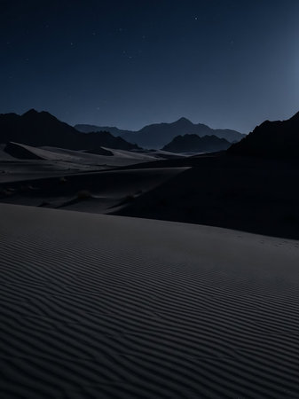 A dark desert landscape unfolds under a clear night sky filled with stars. Silhouetted mountains form the horizon above undulating sand dunes, creating a serene and vast atmosphere.の素材