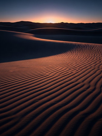 Undulating sand dunes sculpted by wind, casting deep shadows and illuminated by the warm, golden light of sunset. The intricate ripple patterns create a texture.の素材