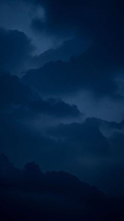 Dark blue clouds swirl and overlap creating a dramatic and moody atmosphere. The lighting suggests a stormy night sky with deep shadows and subtle highlights.の素材