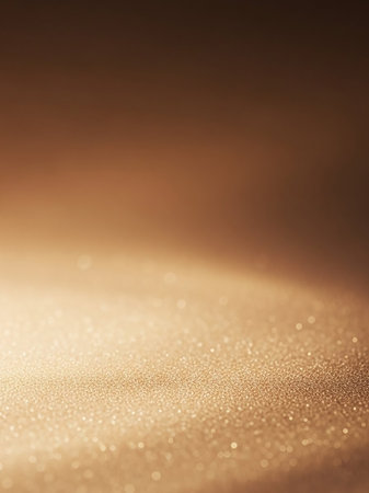 A close-up view of golden sand particles illuminated by soft light, creating a warm, shimmering texture with a bokeh effect.の素材