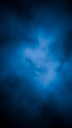 Abstract background with ethereal blue light illuminating through dark, smoky clouds. The contrast creates a mysterious and atmospheric effect with a luminous, diffused glow.の素材