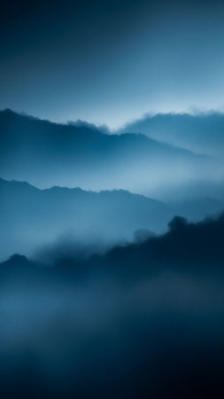 Layers of misty blue mountain ranges fade into the distance, creating a serene and atmospheric landscape under soft, diffused light.の素材