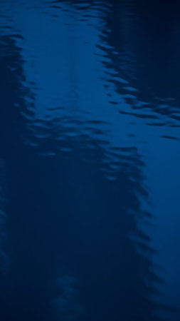 A close-up view of a deep blue water surface with gentle ripples and subtle light reflections, creating an abstract and calming texture.の素材