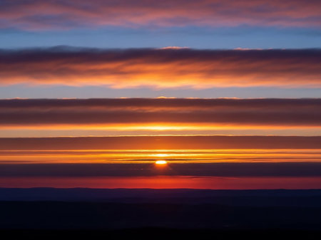 Horizon. showing a sunset with vibrant orange and red hues paints the sky in horizontal bands of color above a dark silhouetted landscape with a bright sun on the...の素材