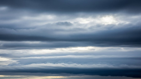 A dense, layered formation of dark grey and white clouds stretches across the frame, creating a moody, overcast sky with diffused light.の素材
