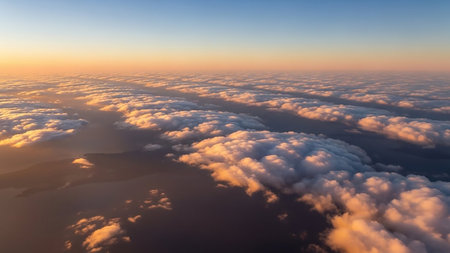 Aerial view of white clouds in parallel rows illuminated by golden sunrise light over dark land and water, creating a vast atmospheric landscape.の素材