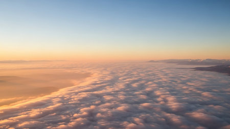 Aerial view of a sea of fluffy white and golden clouds illuminated by warm sunrise light, with a clear blue sky above.の素材