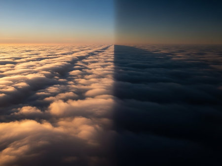 A dramatic aerial view a vast expanse of clouds divided by a sharp line between golden sunrise light and deep shadow.の素材