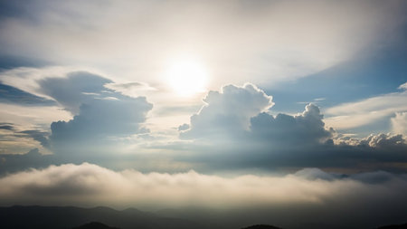 Bright sun illuminates dramatic cumulus clouds and silhouetted mountain peaks, creating a serene and atmospheric dawn landscape.の素材