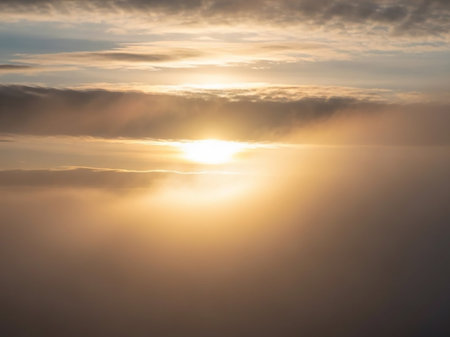 Meteorological showing bright golden sun breaking through dense atmospheric clouds and mist creating a radiant and ethereal light effect with warm tones keywords:...の素材