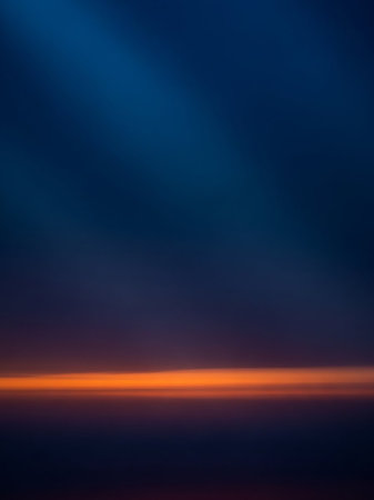 Horizontal showing dark blue sky background with a vibrant orange horizontal light streak near the horizon and diagonal light rays emanating from the upper left....の素材