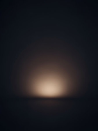 A dark studio backdrop is subtly lit by a soft, warm spotlight on the floor, creating an empty, atmospheric space with a gentle gradient.の素材