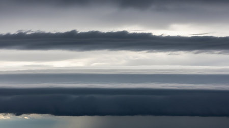 Distinct horizontal layers of dark gray and light gray clouds form a striated pattern across a muted, overcast sky.の素材