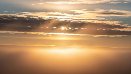 Golden sun rays break through grey clouds, creating a luminous, hazy golden glow above a bright horizon.の素材