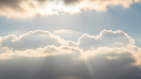 Soft golden sunbeams illuminate fluffy white clouds against a pale blue sky, creating a serene and ethereal atmosphere with gentle light filtering through.の素材