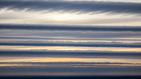 Horizontal showing horizontal layers of wispy gray clouds with soft yellow and orange light peeking through at sunset or sunrise creating a dramatic and textured...の素材
