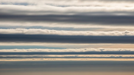 Distinct horizontal bands of dark gray and white clouds form a striped, layered pattern against a pale sky.の素材
