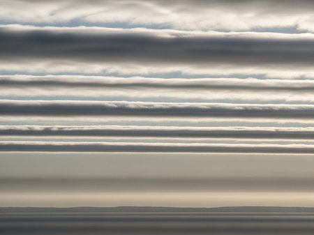 Muted showing horizontal cloud formations layered across a vast expanse of calm ocean under a bright sky creating a serene and dramatic natural landscape scene...の素材