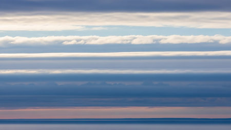 Horizontal bands of blue and white clouds are layered above a calm ocean, creating a serene, abstract natural pattern.の素材